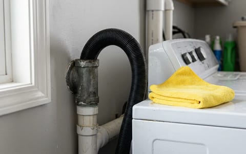 Close-up of a washing machine discharge hose inserted into a laundry room wall standpipe