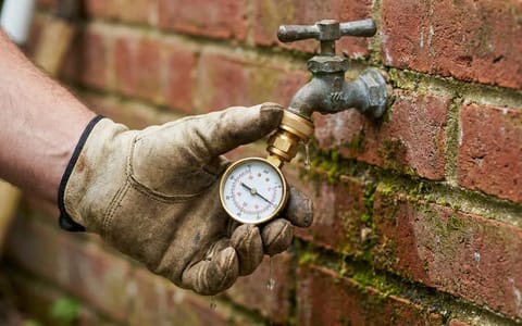Homeowner checking residential water pressure with a gauge on an outdoor spigot.