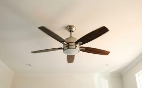 A modern ceiling fan spinning counterclockwise to provide cooling airflow in a sunlit room.