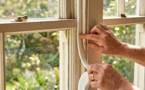 Homeowner applying new adhesive weatherstripping to a window frame