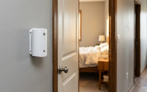 A carbon monoxide detector installed on a hallway wall outside a bedroom