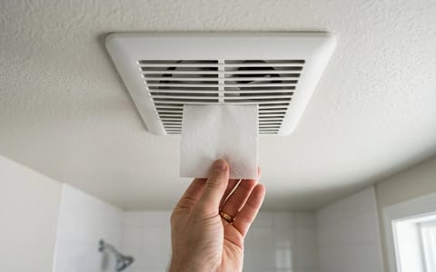 A person performing the toilet paper suction test on a bathroom ceiling exhaust fan.