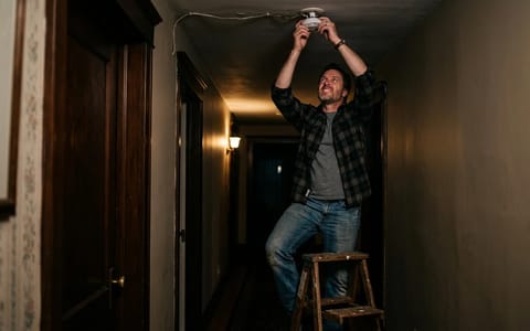 Homeowner reaching up to remove a smoke detector from the ceiling
