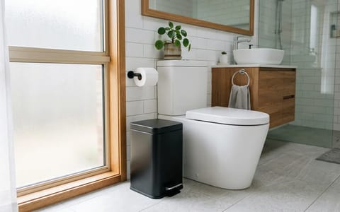 A modern bathroom showing a trash can placed next to the toilet to discourage flushing non-degradable items.