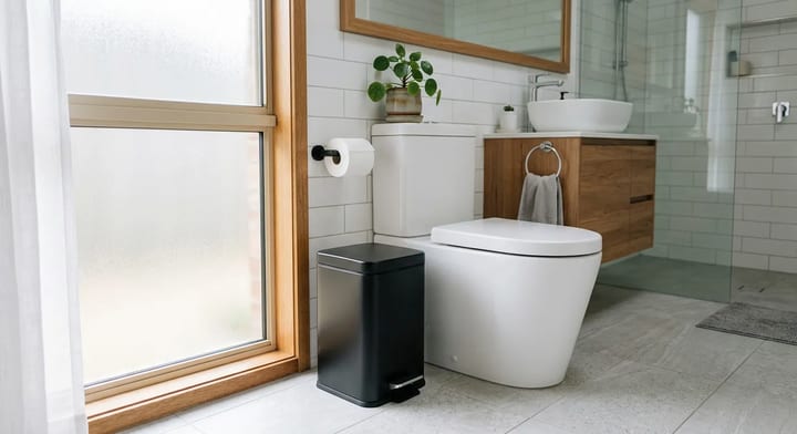 A modern bathroom showing a trash can placed next to the toilet to discourage flushing non-degradable items.