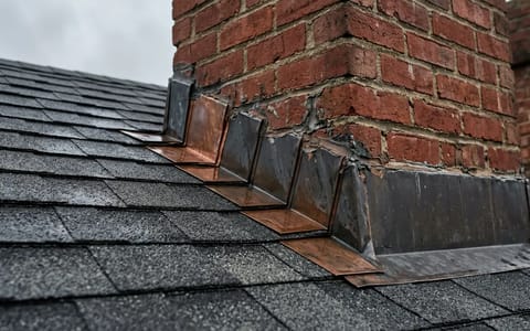 Brick chimney on an asphalt shingle roof showing the metal flashing at the base