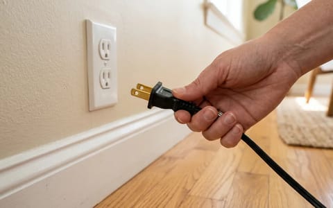 Hand holding an electrical plug recently removed from a wall outlet