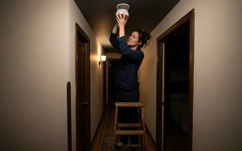 Homeowner removing a chirping smoke detector from the ceiling at night.