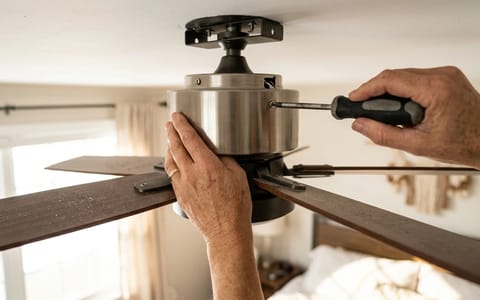 Homeowner using a screwdriver to tighten the canopy of a ceiling fan