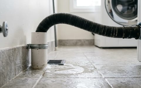 Washing machine discharge hose backing up and spilling water onto a tiled laundry room floor