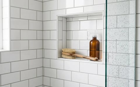 Clean shower tiles and grout with a scrub brush resting on a shower niche.