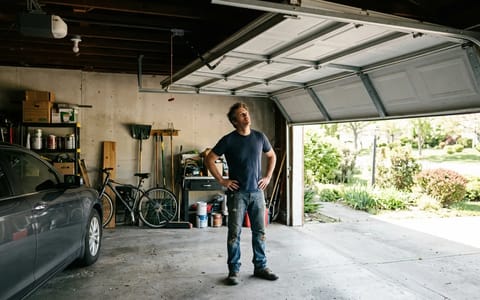 A homeowner looking at a partially open garage door that refuses to close.